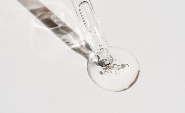 A clear drop of liquid with air bubbles falling from a dropper onto a white surface showcasing fluid dynamics ideal for experiments and research in chemistry and biology 4 science applications