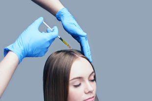 hands applying treatment for hair restoration on a woman with long hair using a syringe wearing blue gloves hair growth therapy 3 solutions