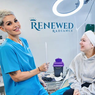 A professional aesthetician holding a treatment tool smiles at a client in a clinic setting featuring branding for Renewed Radiance with a focus on skincare and beauty. Two individuals engage in a positive consultation about skin rejuvenation options.