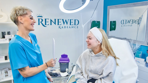 two women interacting in a skincare clinic one woman receiving treatment smiling while the other holds a skin care tool focus on beauty and skincare routines