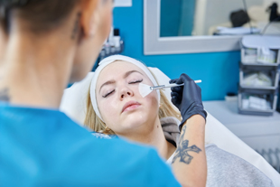 aesthetic treatment session with a professional applying facial product to a female client in a skincare clinic focused on beauty treatments and rejuvenation techniques