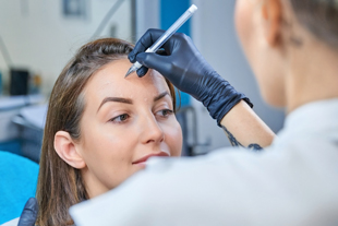 a cosmetologist applying semi-permanent makeup to a woman's eyebrows with a tattoo pen in a modern beauty salon enhancing brows with precision 14 techniques